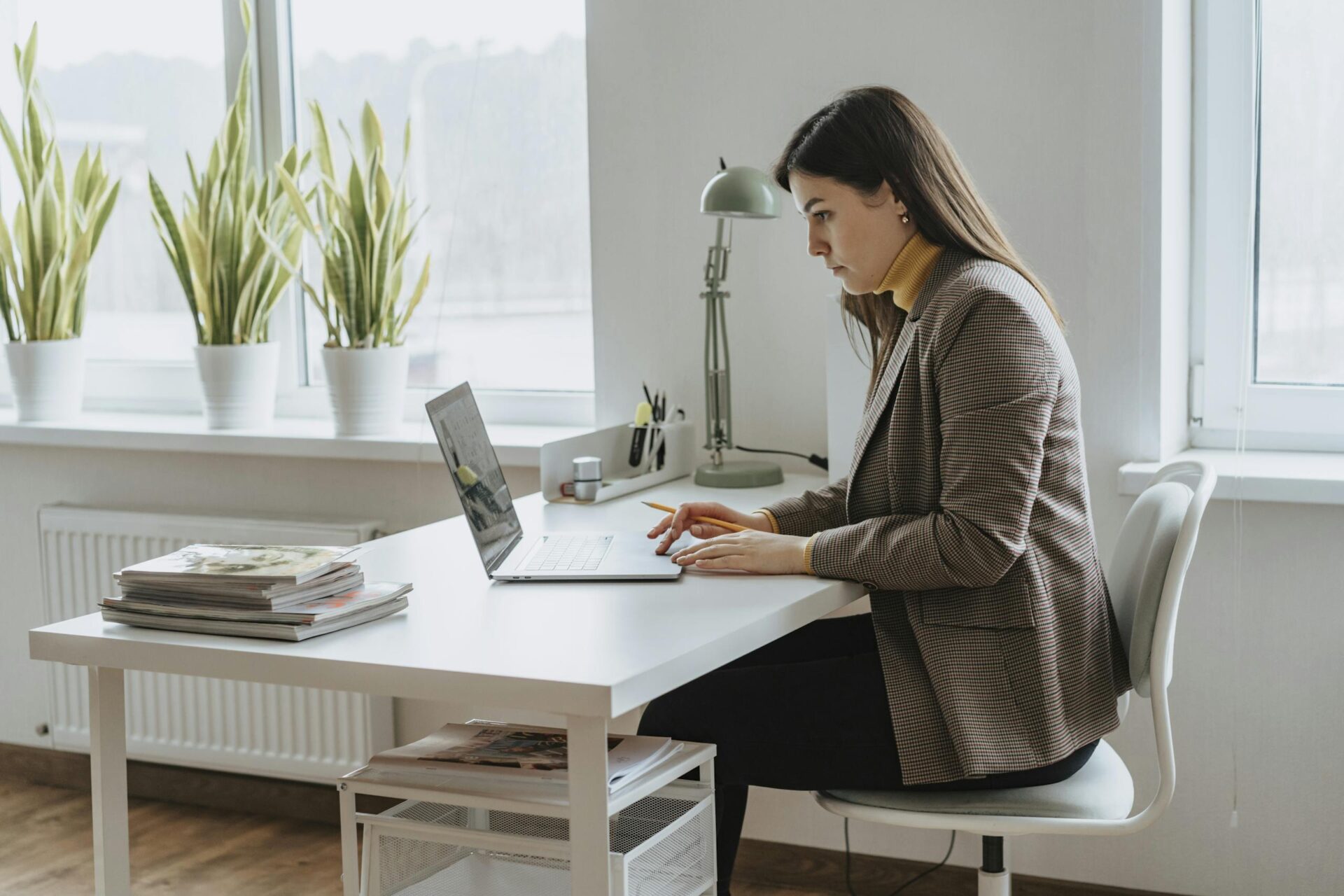 A focused woman works on a laptop in a bright modern office with plants.